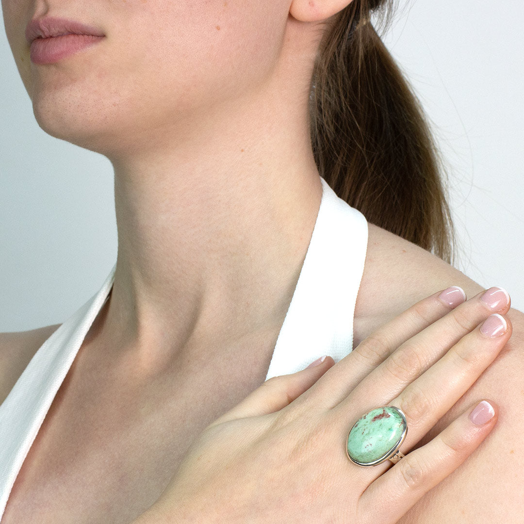 Woman wearing a silver ring with green and red gemstone against a plain background