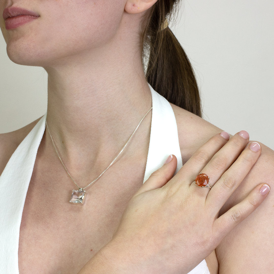 Woman wearing a silver ring with an orange gemstone on a plain background