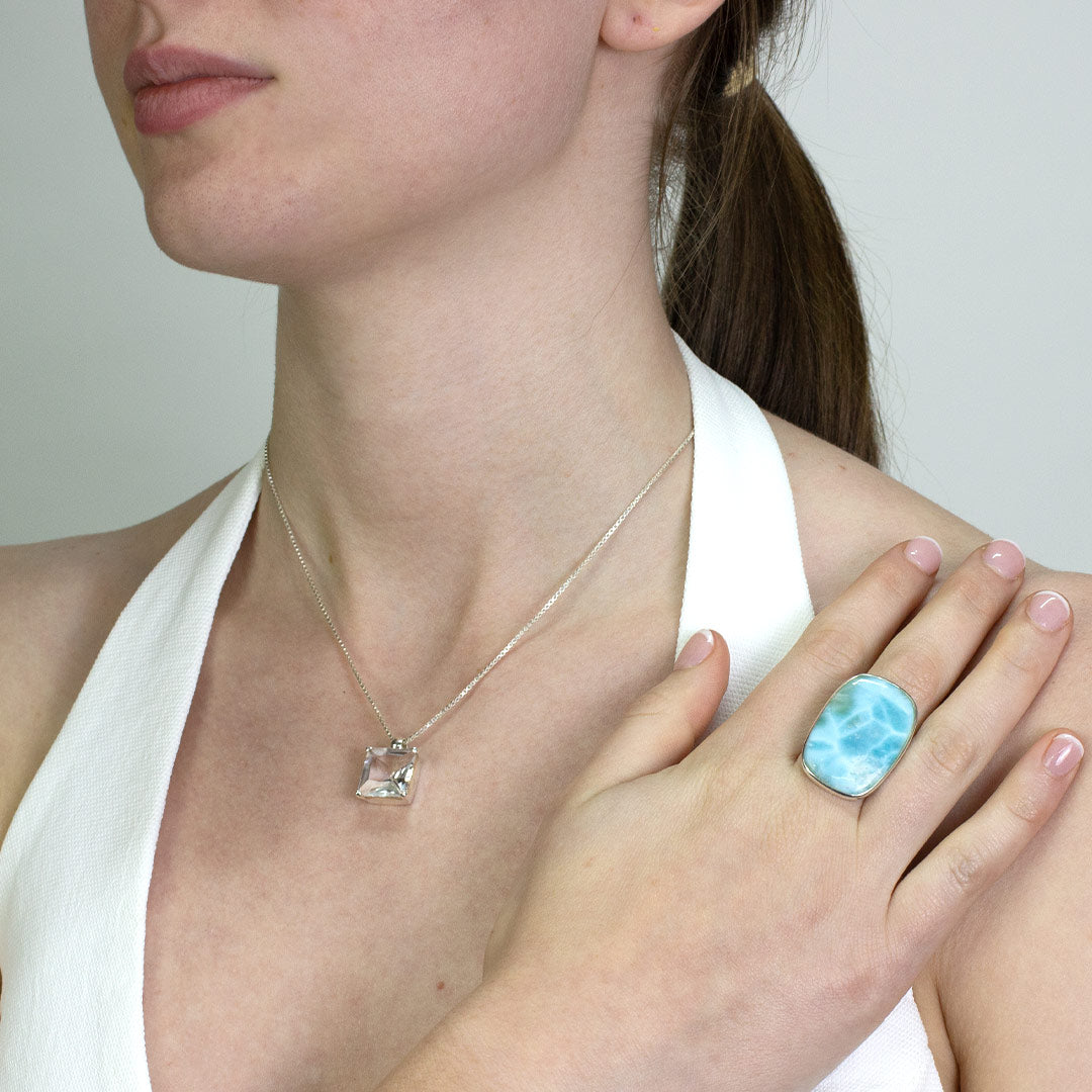 Woman wearing a silver ring with a light blue gemstone on a plain background.