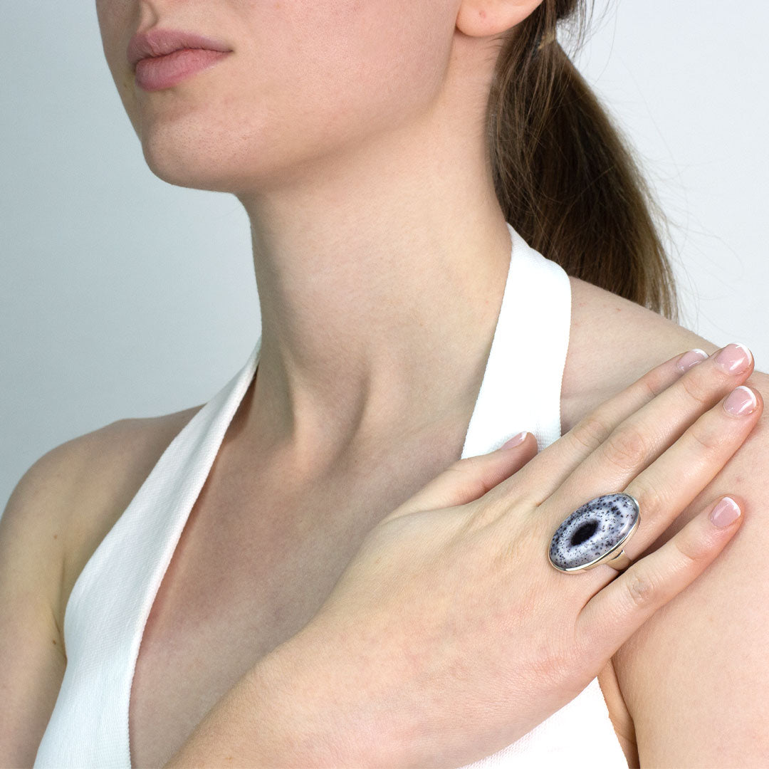 Woman wearing a silver ring with a speckled stone on a plain background