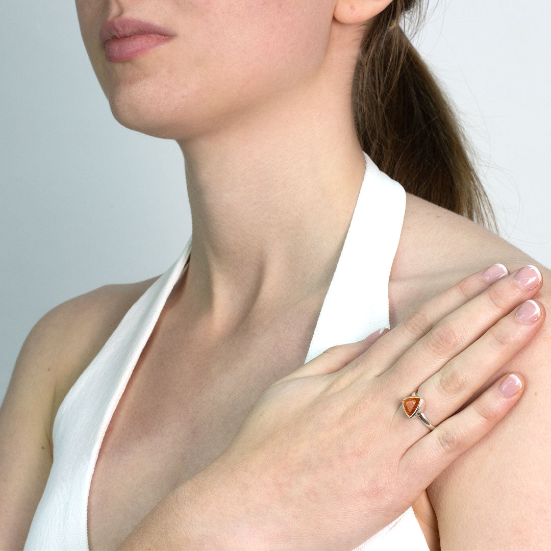 Woman wearing a silver ring with a triangular orange stone on a plain background