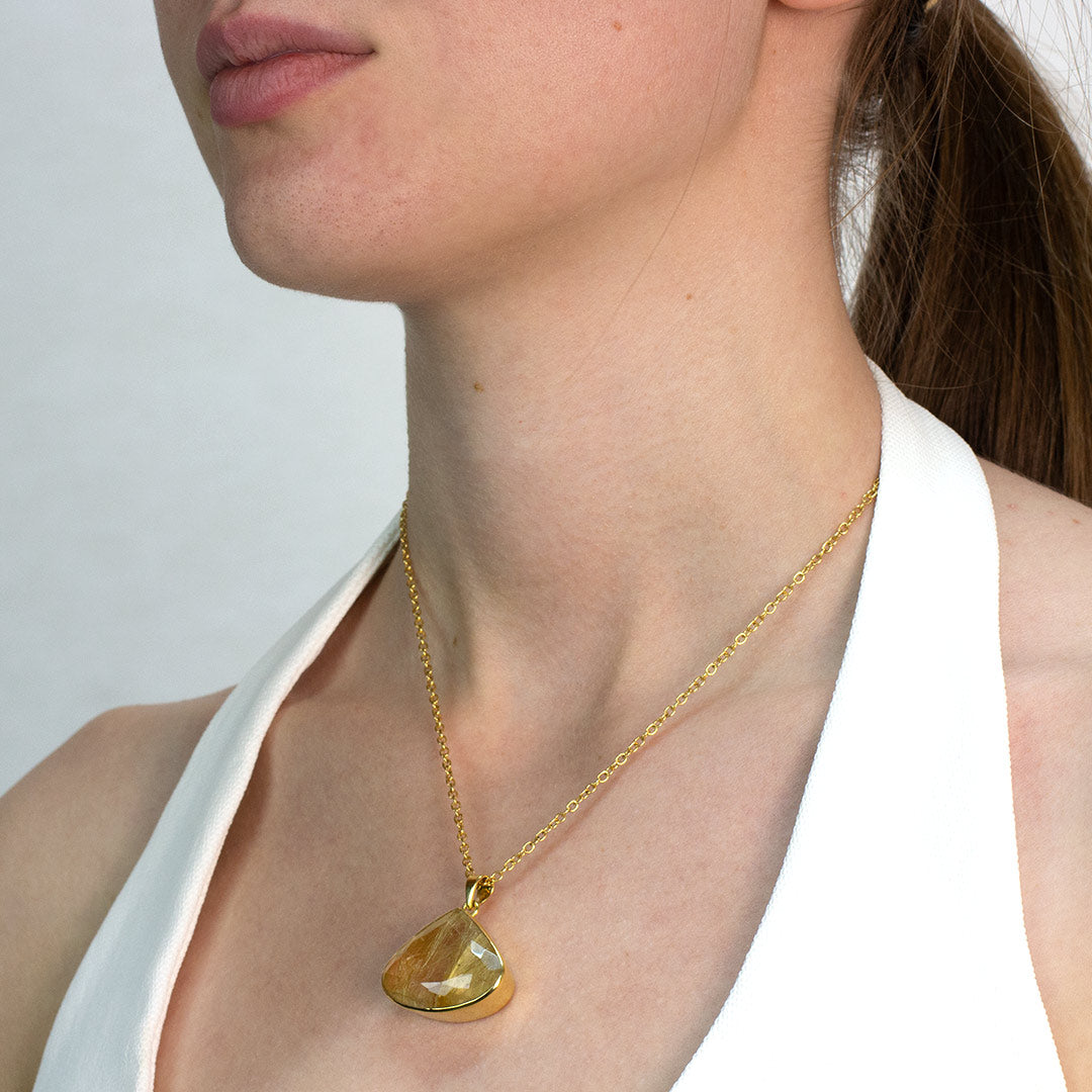 Woman wearing a golden necklace with a clear stone on a plain background