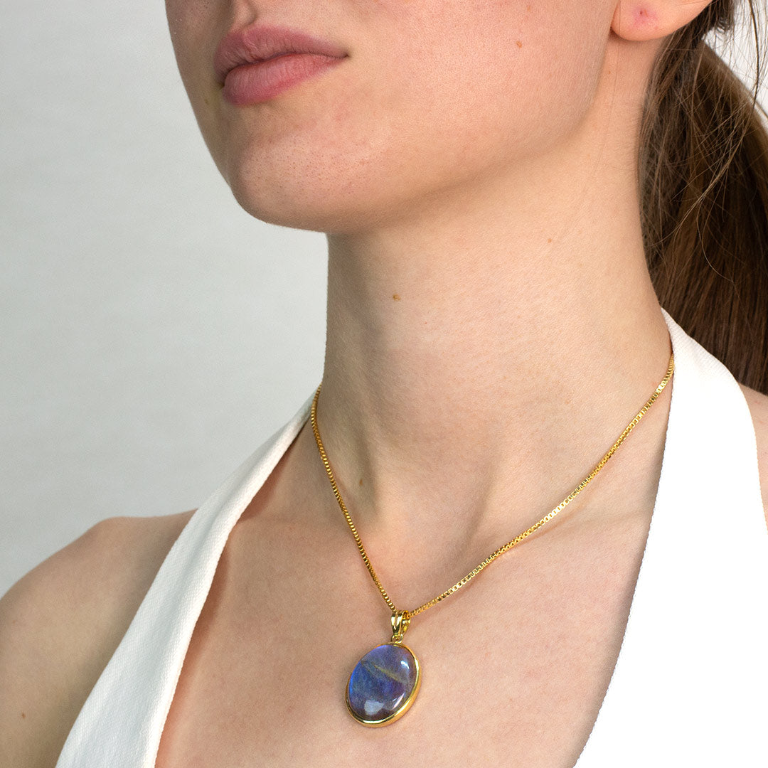 Woman wearing a golden necklace with a blue pendant against a neutral background
