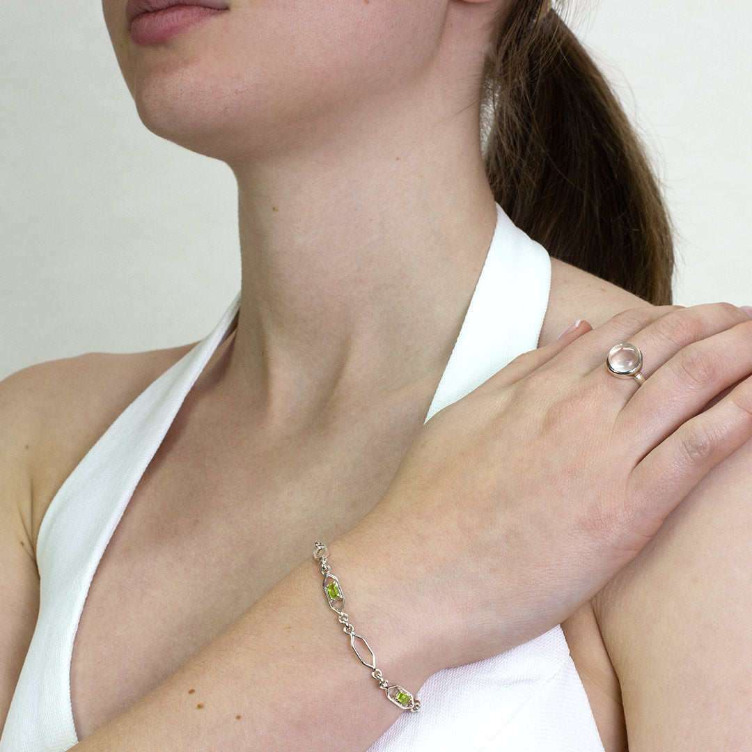 Woman wearing a silver bracelet with green gemstones on a plain background