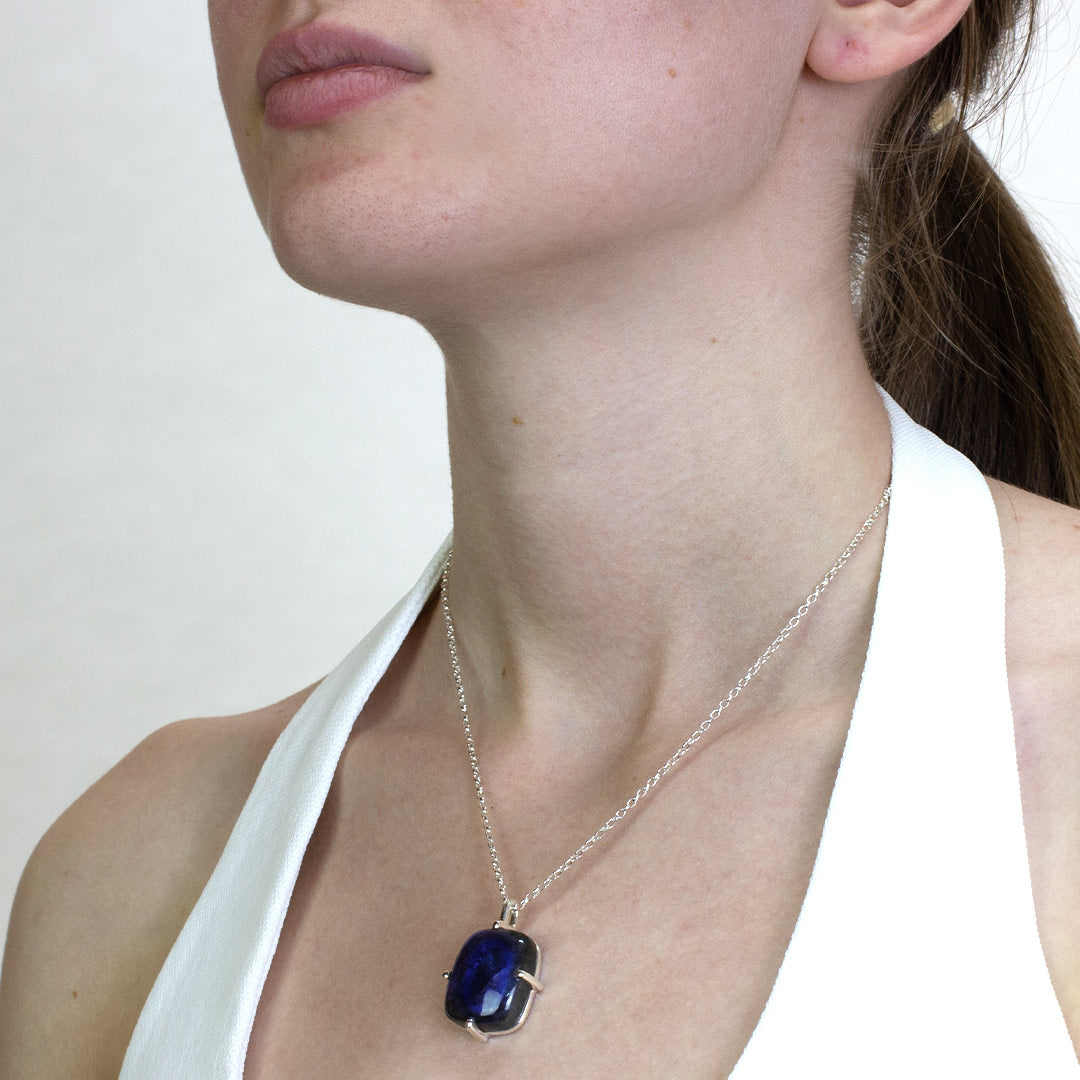 Woman wearing a necklace with a blue gemstone on a plain background