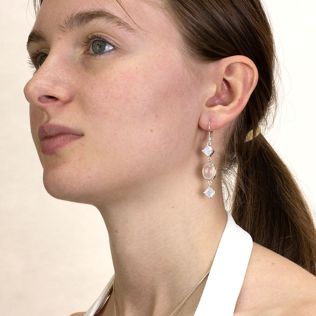 Close-up of a woman wearing a silver drop earring with pink and iridescent gemstones on a plain background