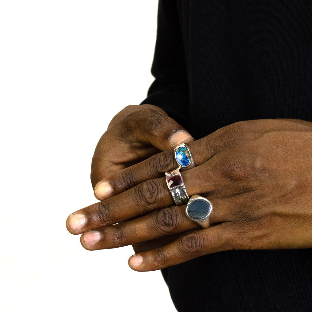 Close-up of a person's hands with a silver ring with a green and blue gemstone on a plain background