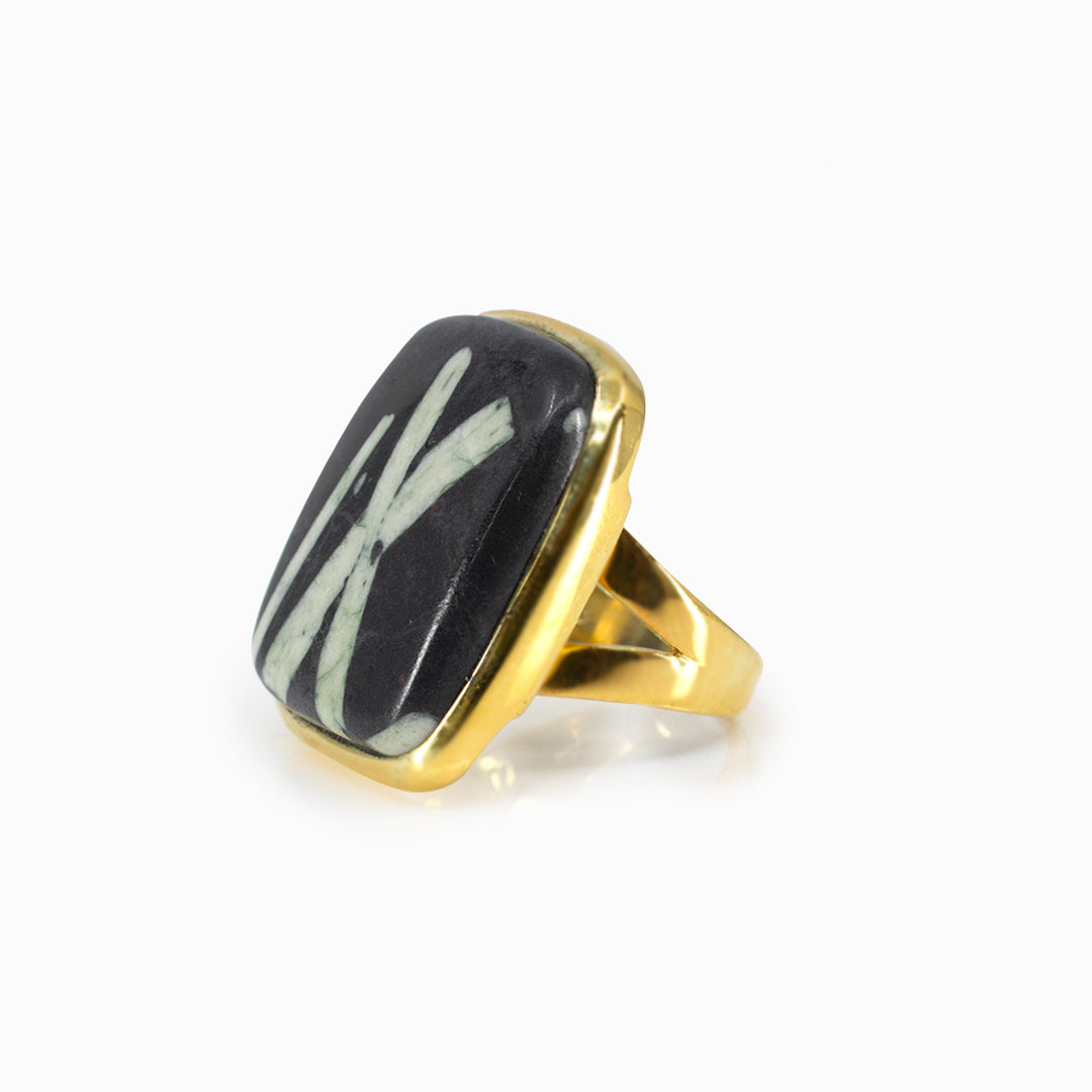 Golden ring with a black rectangular stone with white lines on a white background
