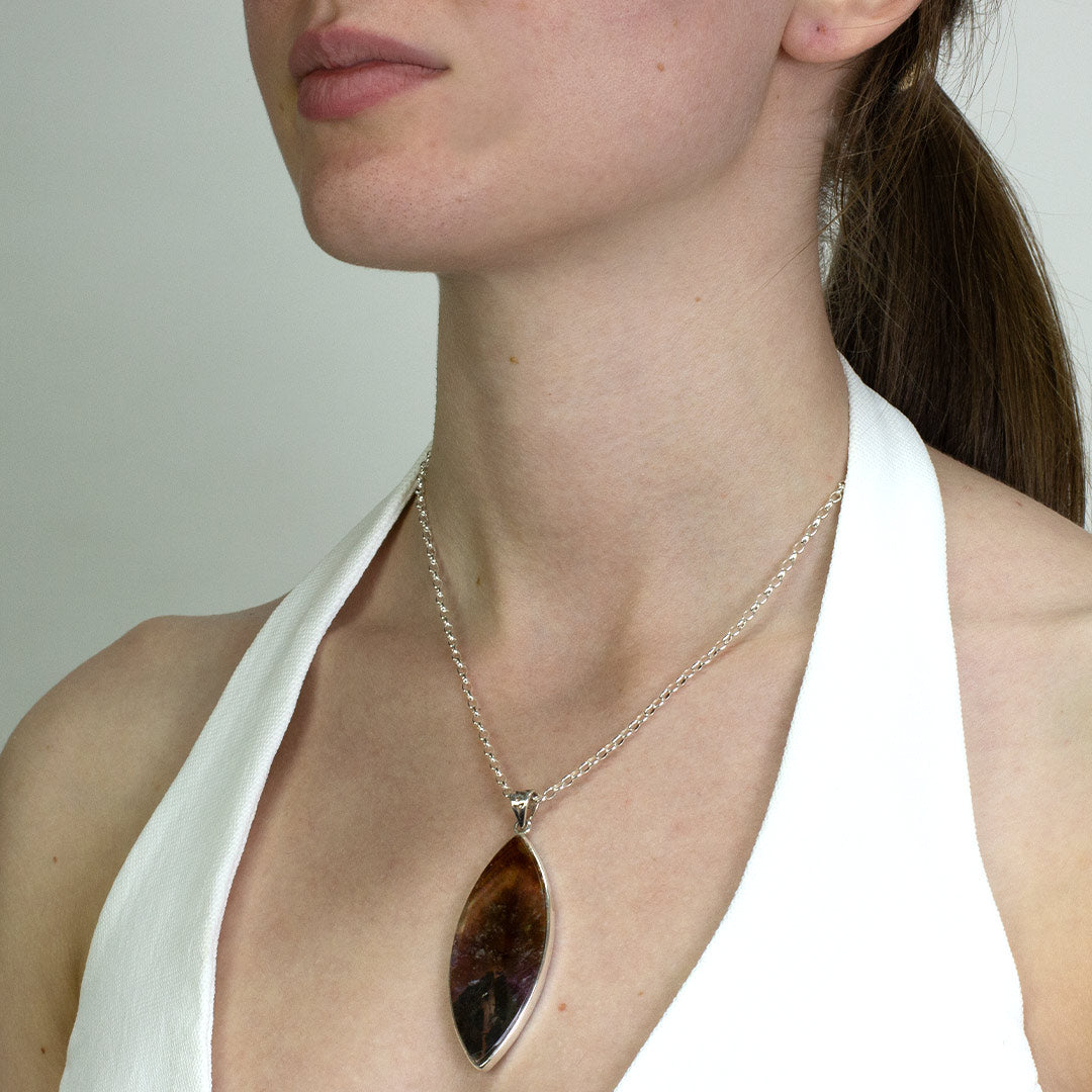 Woman wearing a marquise-shaped gemstone pendant on a silver chain against a plain background