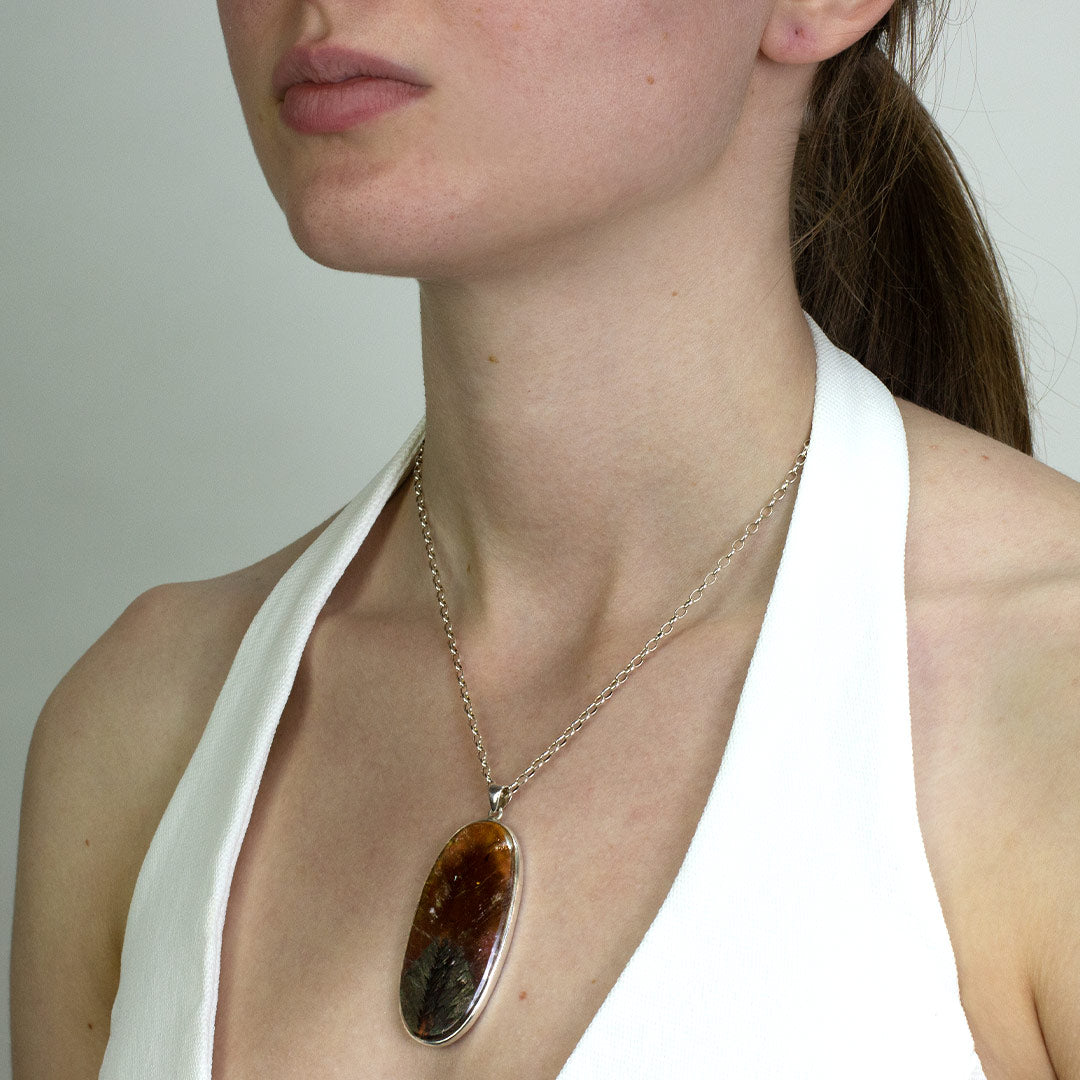 Woman wearing a silver necklace with a large oval pendant on a plain background
