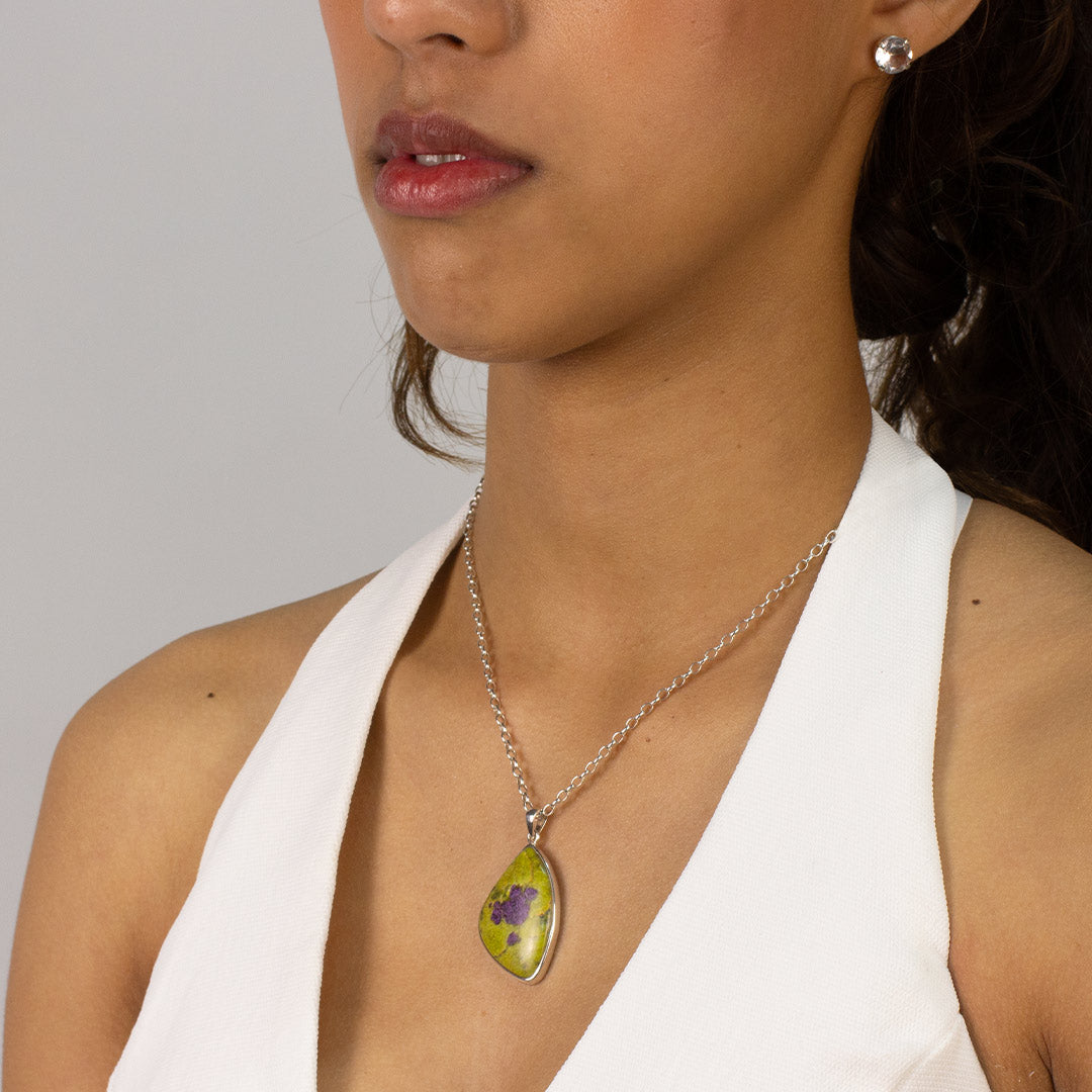 Woman wearing a silver freeform necklace with green and purple stone on a plain background
