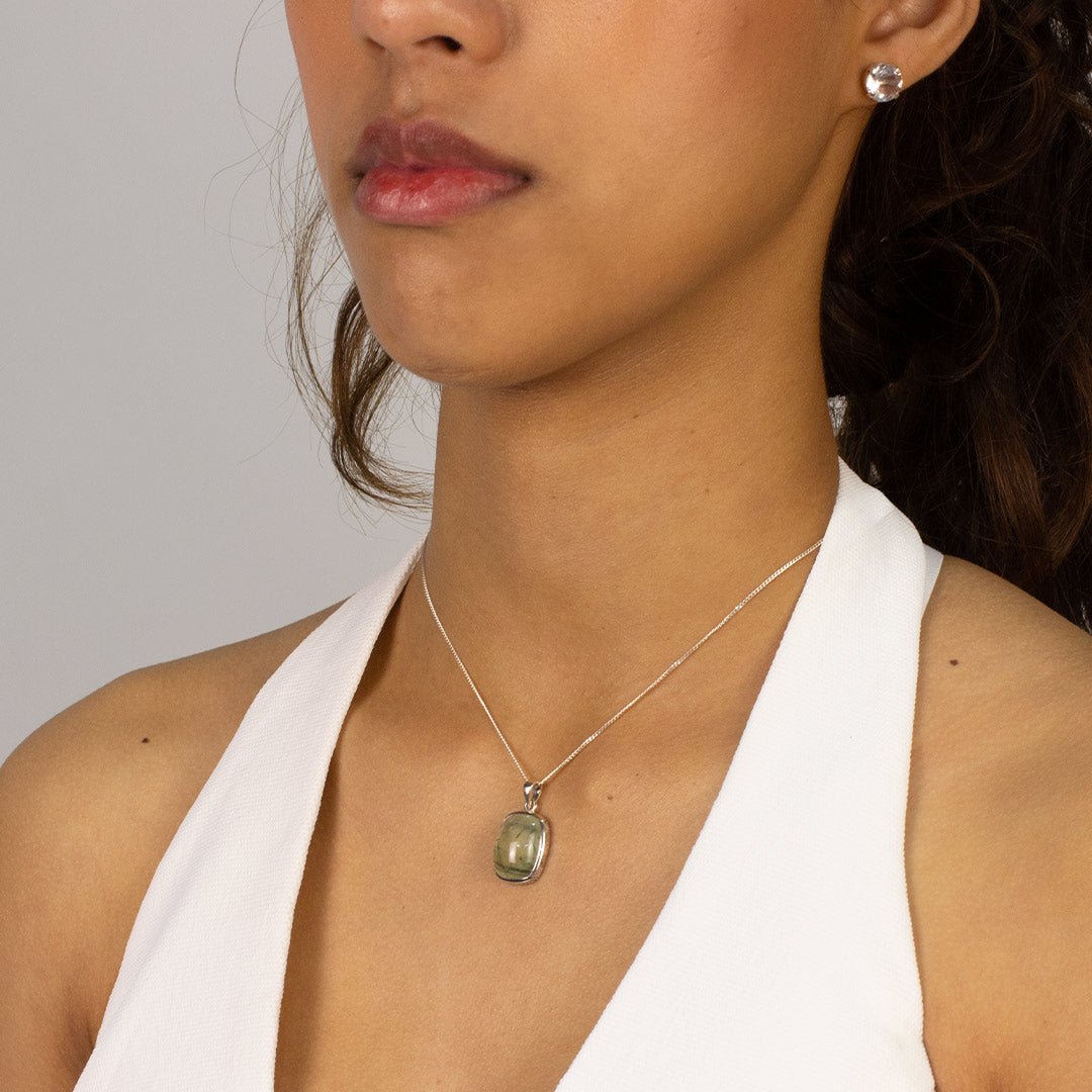 Woman wearing a silver necklace with a green stone pendant on a plain background