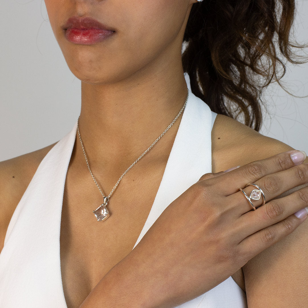 Woman wearing a silver ring with a freeform clear gemstone on a plain background