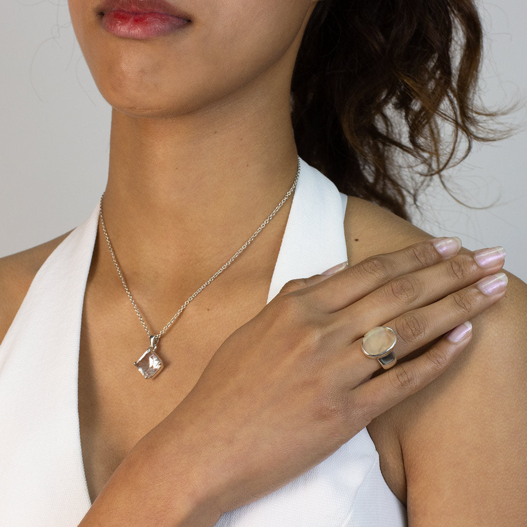 Woman wearing a silver ring with a light-colored stone on a plain background