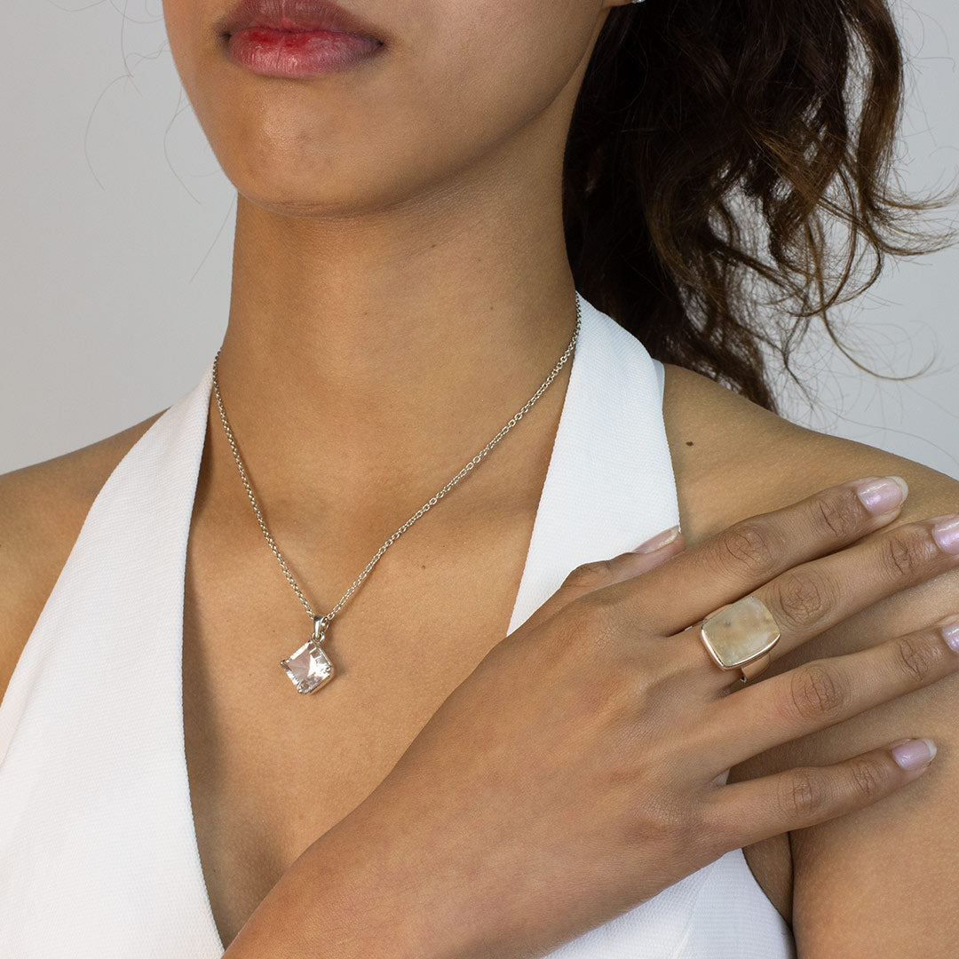 Woman wearing a silver ring with a sheer stone on a plain background
