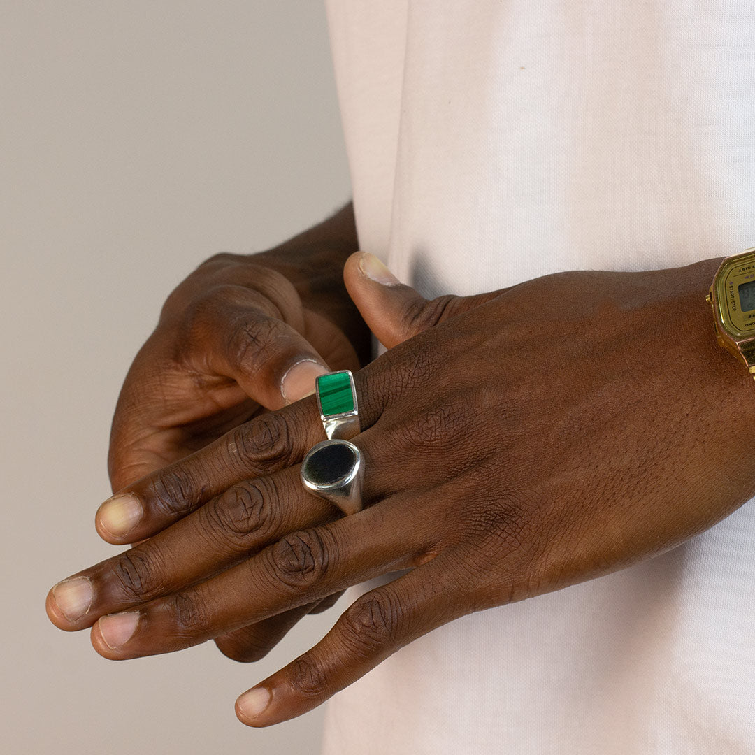 Hand wearing a silver ring with a dark stone on a plain background