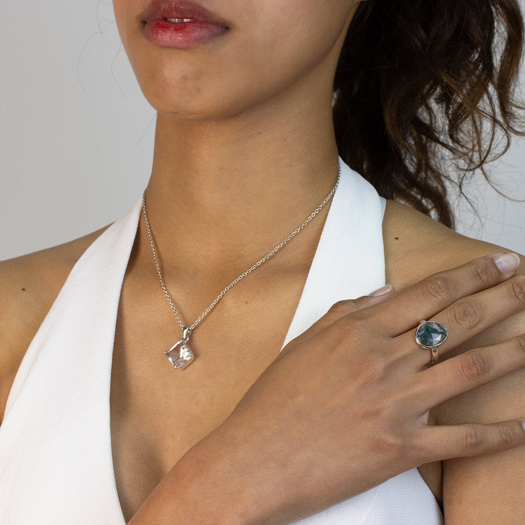 Woman wearing a silver ring with a green marbled stone on a plain background