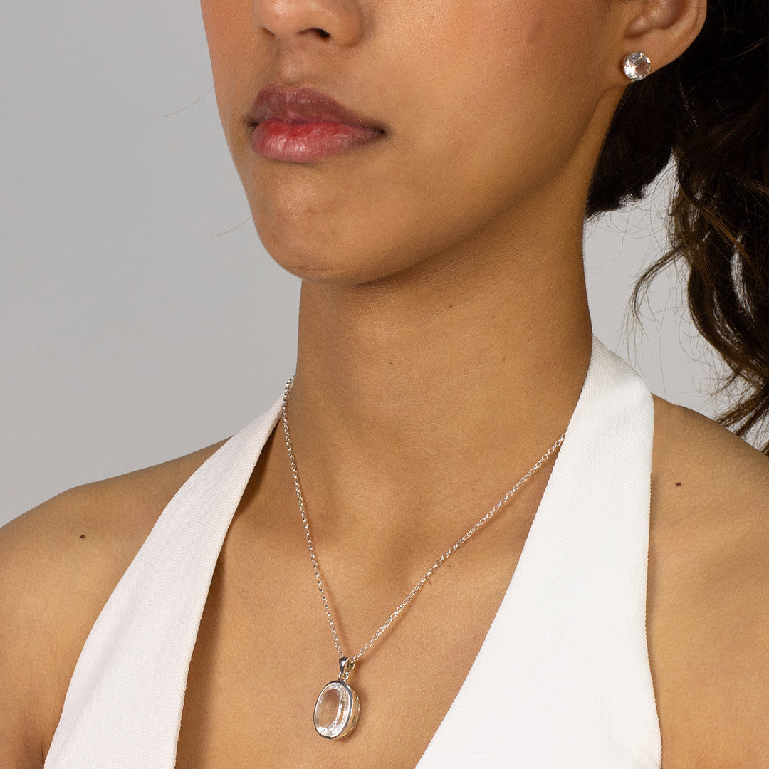 Woman wearing a silver pendant with a clear gemstone on a plain background
