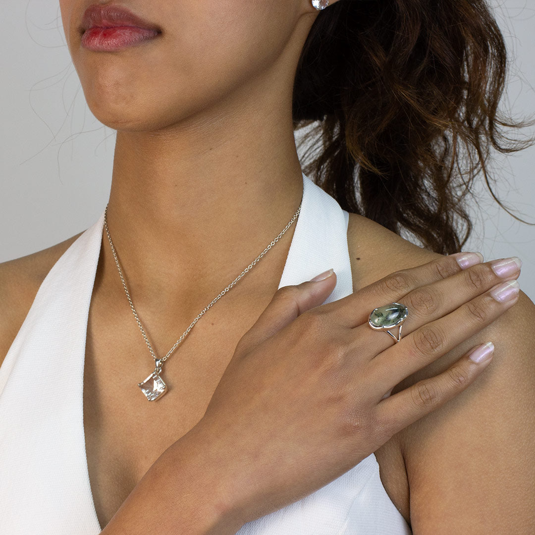 Woman wearing a silver silver ring with a green stone on a plain background