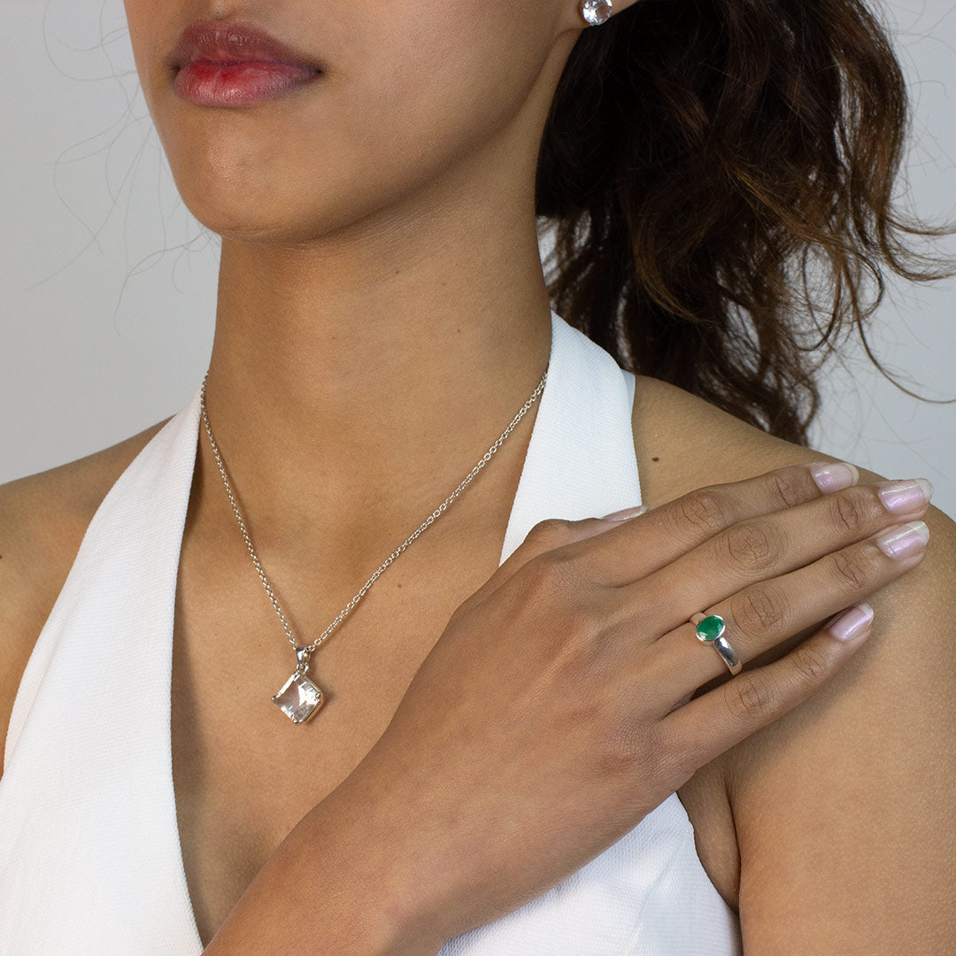 Woman wearing a silver ring with a green gemstone on a plain background