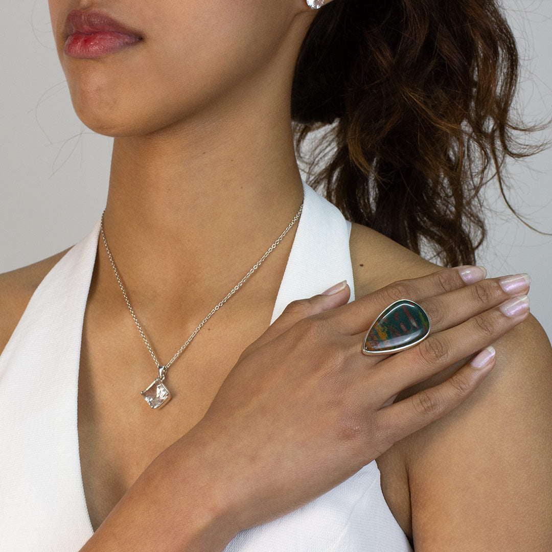 Woman wearing a silver ring with a teardrop-shaped gemstone on a plain background