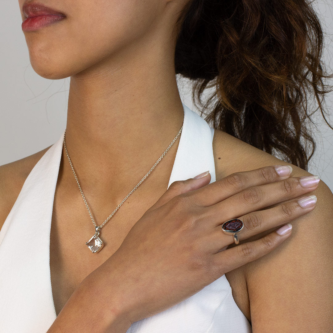 Woman wearing a silver ring with freeform druzy stone on a plain background