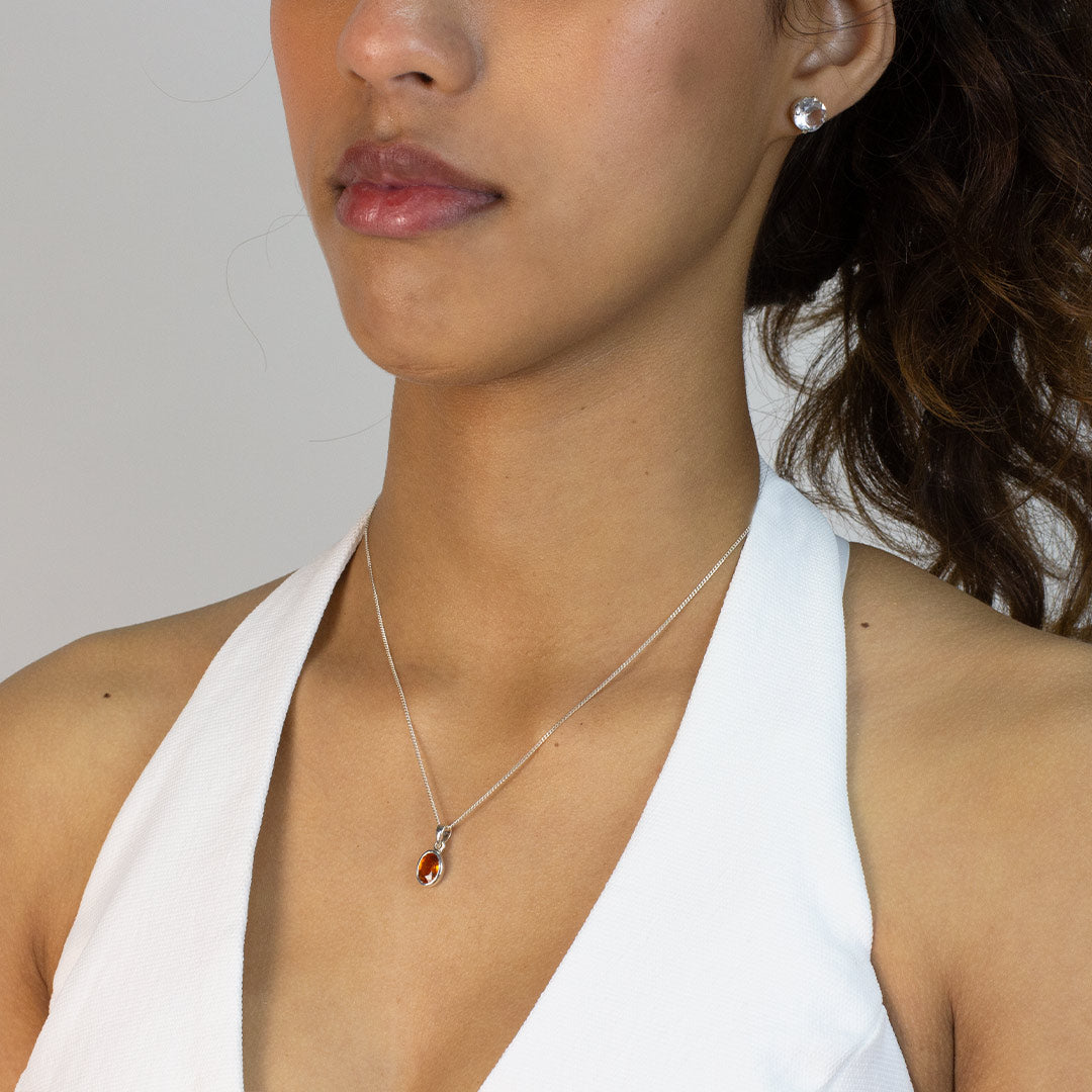 Woman wearing a silver necklace with a pendant featuring an orange gemstone on a plain background