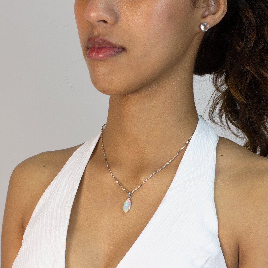 Woman wearing a necklace with a pendant featuring an opal stone on a plain background