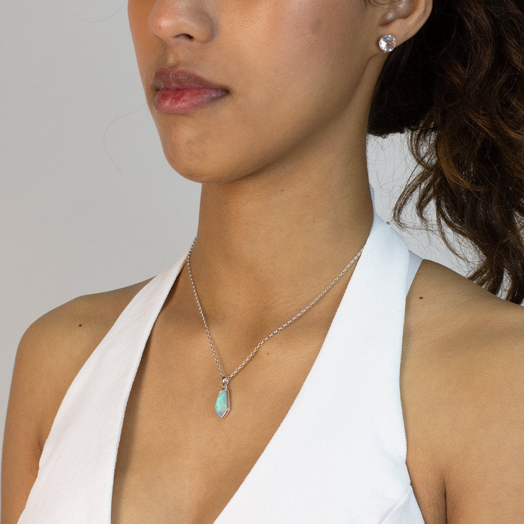 Woman wearing a necklace with a pendant featuring an opal stone on a plain background