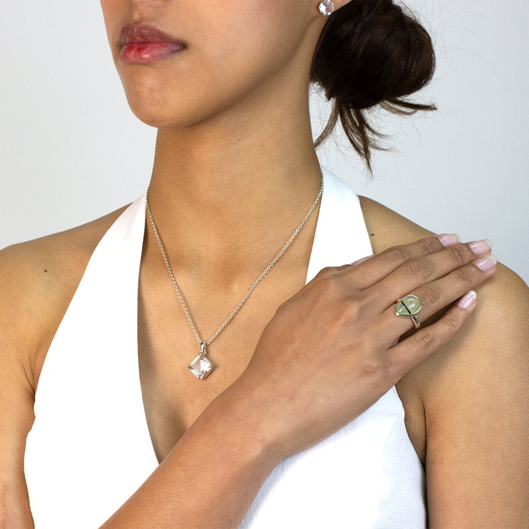 Woman wearing a silver ring with a light green teardrop-shaped gemstone on a plain background