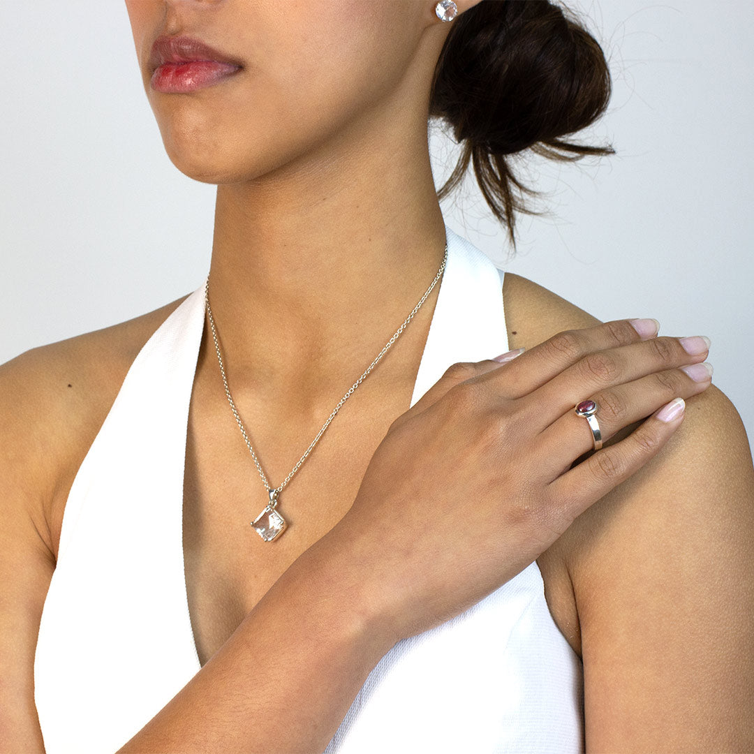 Woman wearing a silver ring with a pink gemstone on a plain background