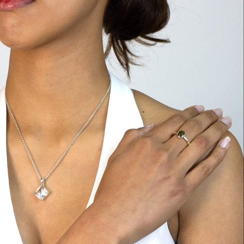 Woman wearing a silver ring with a green gemstone on a plain background