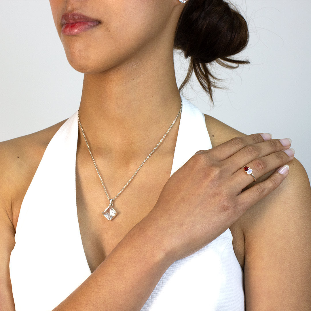 Woman wearing a silver ring with red and clear gemstones on a plain background