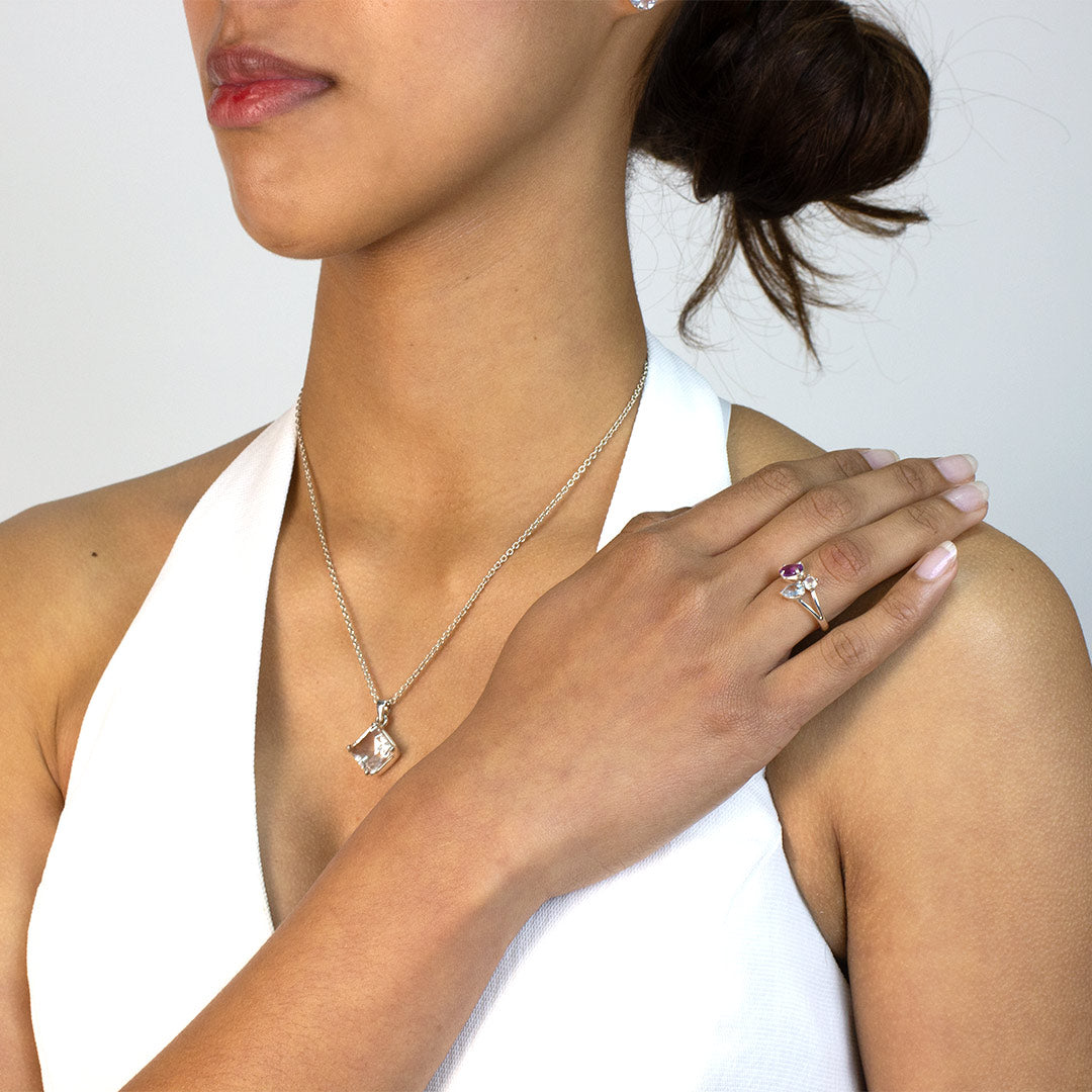 Woman wearing a silver ring with purple, blue and clear gemstones on a plain background