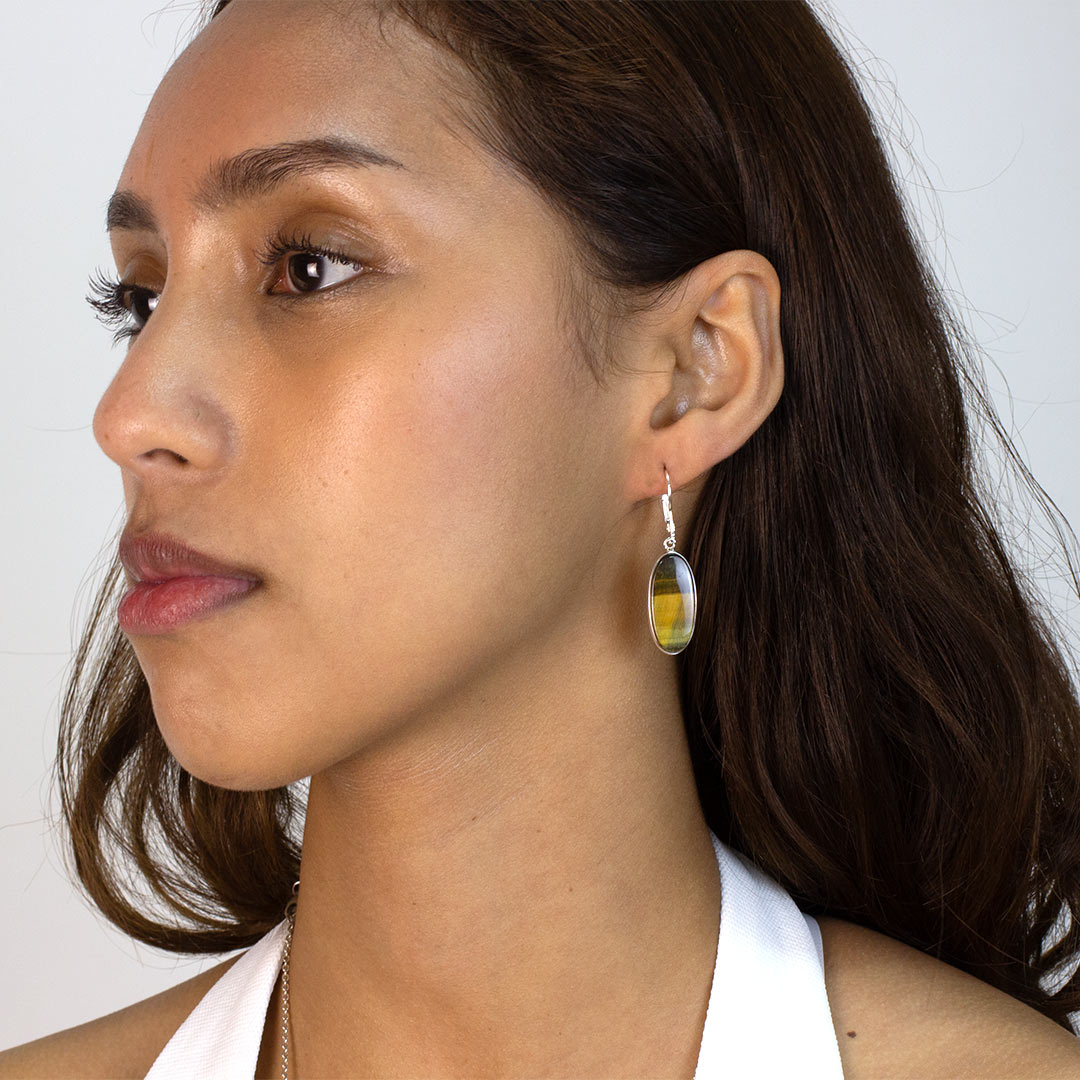 Woman wearing an oval-shaped silver earring with brown stone on a plain background