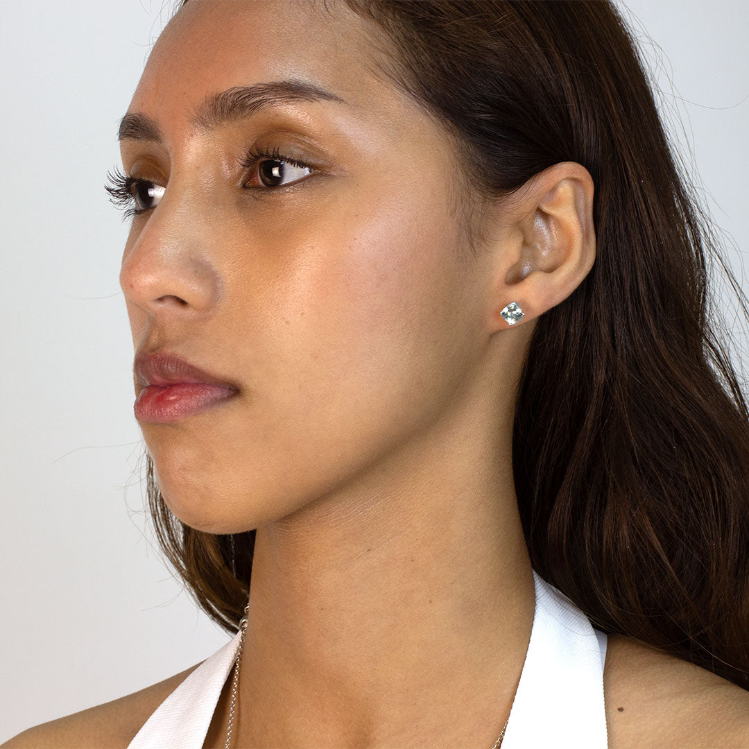 Woman wearing a silver stud earring with blue gemstone on a plain background