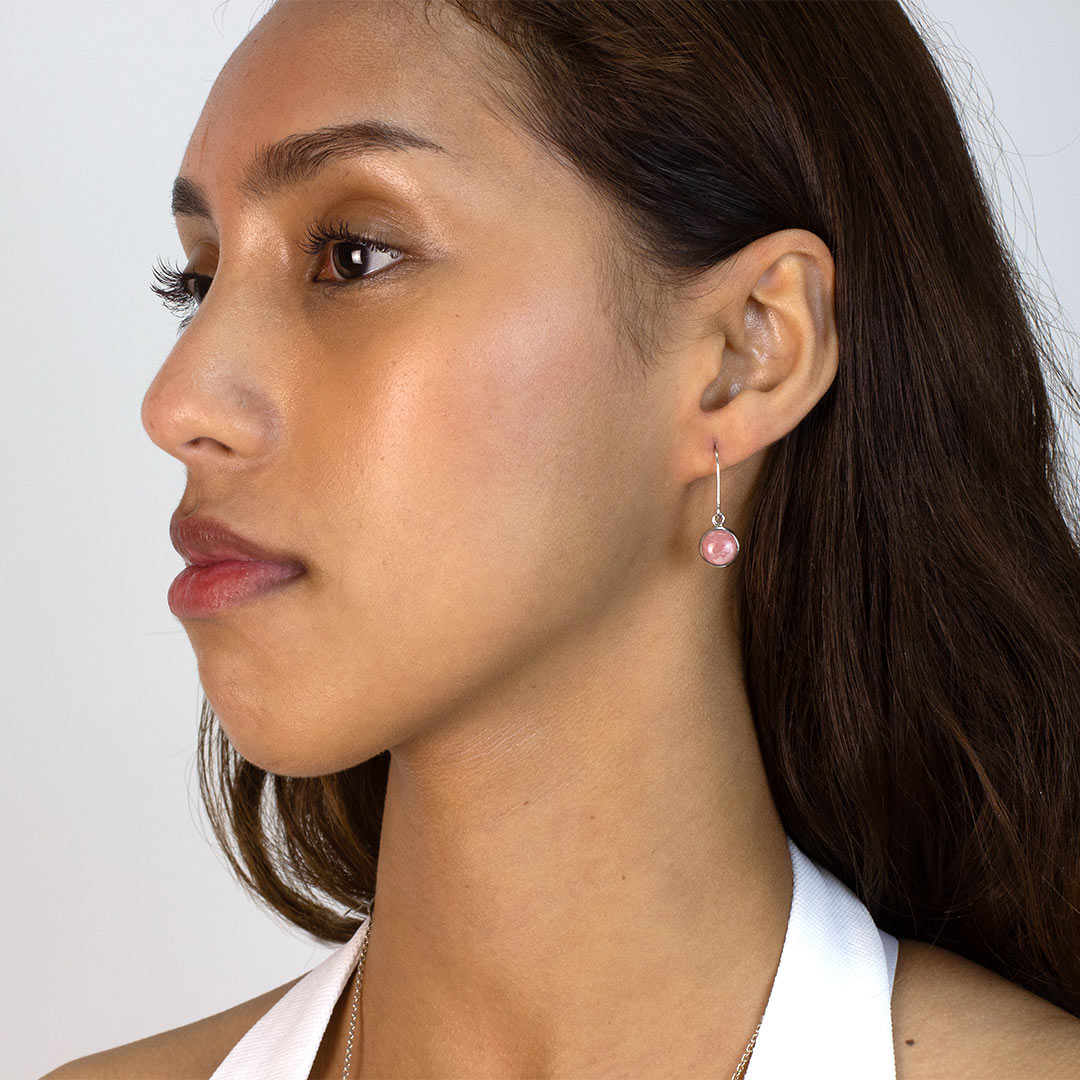 Woman wearing a silver drop earring with pink gemstone on a plain background