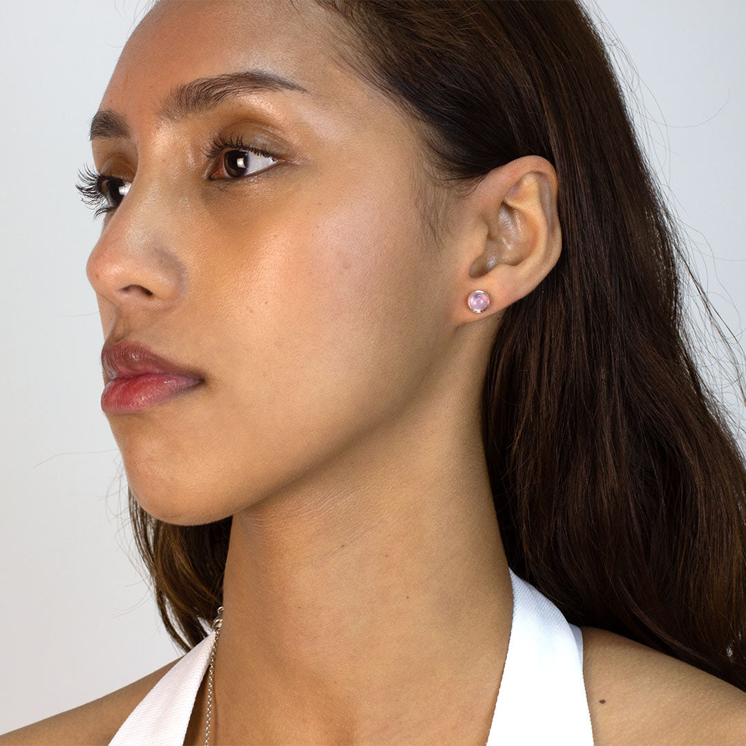 Woman wearing silver stud earring with pink gemstone on a plain background