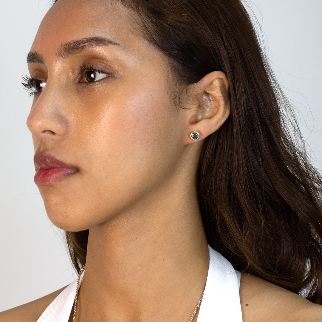 Woman wearing a silver stud earring with green gemstone on a plain background