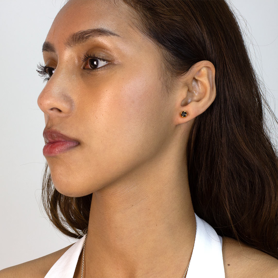 Woman wearing a gold stud earring with brown gemstone on a plain background