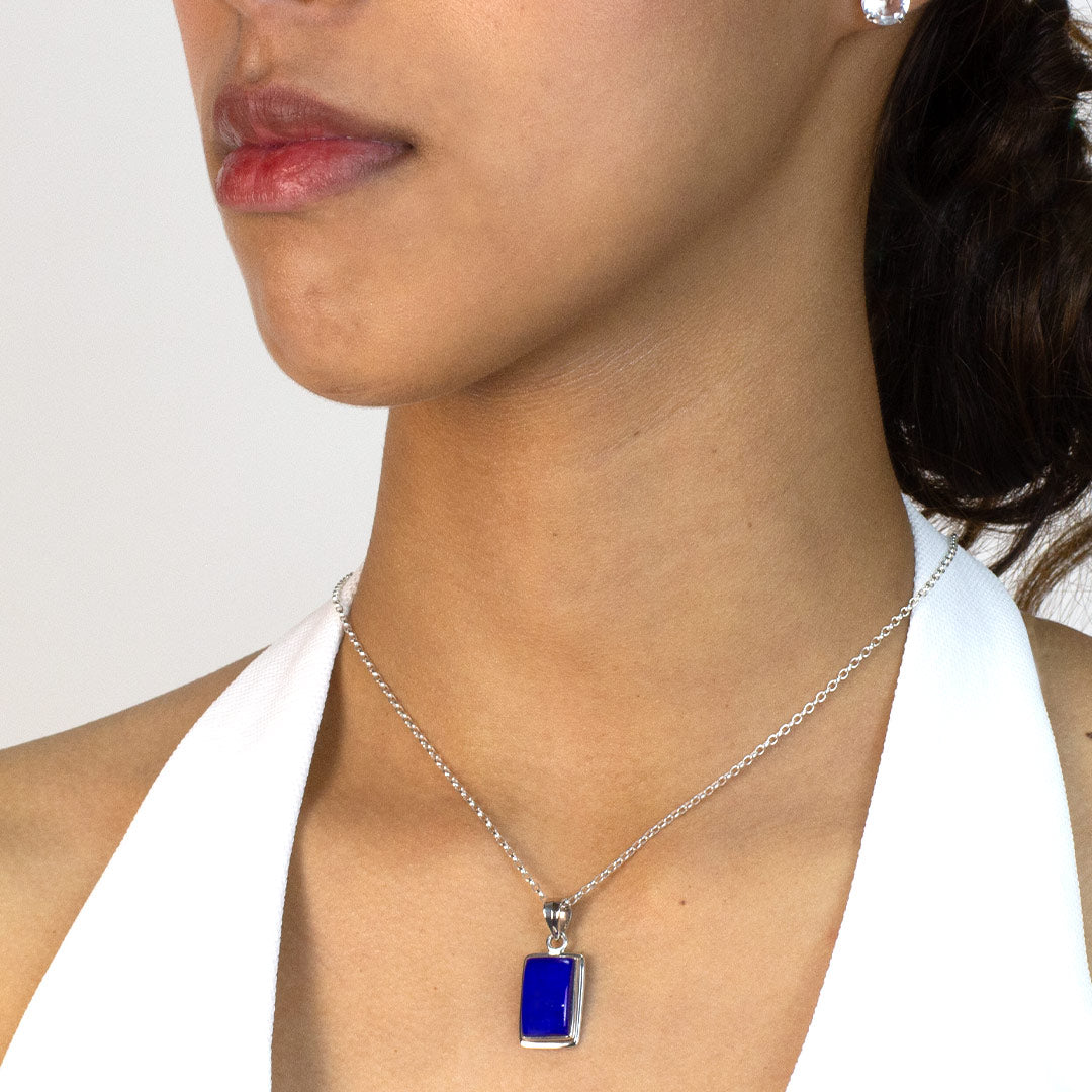 Woman wearing a silver necklace with a blue rectangular pendant on a plain background