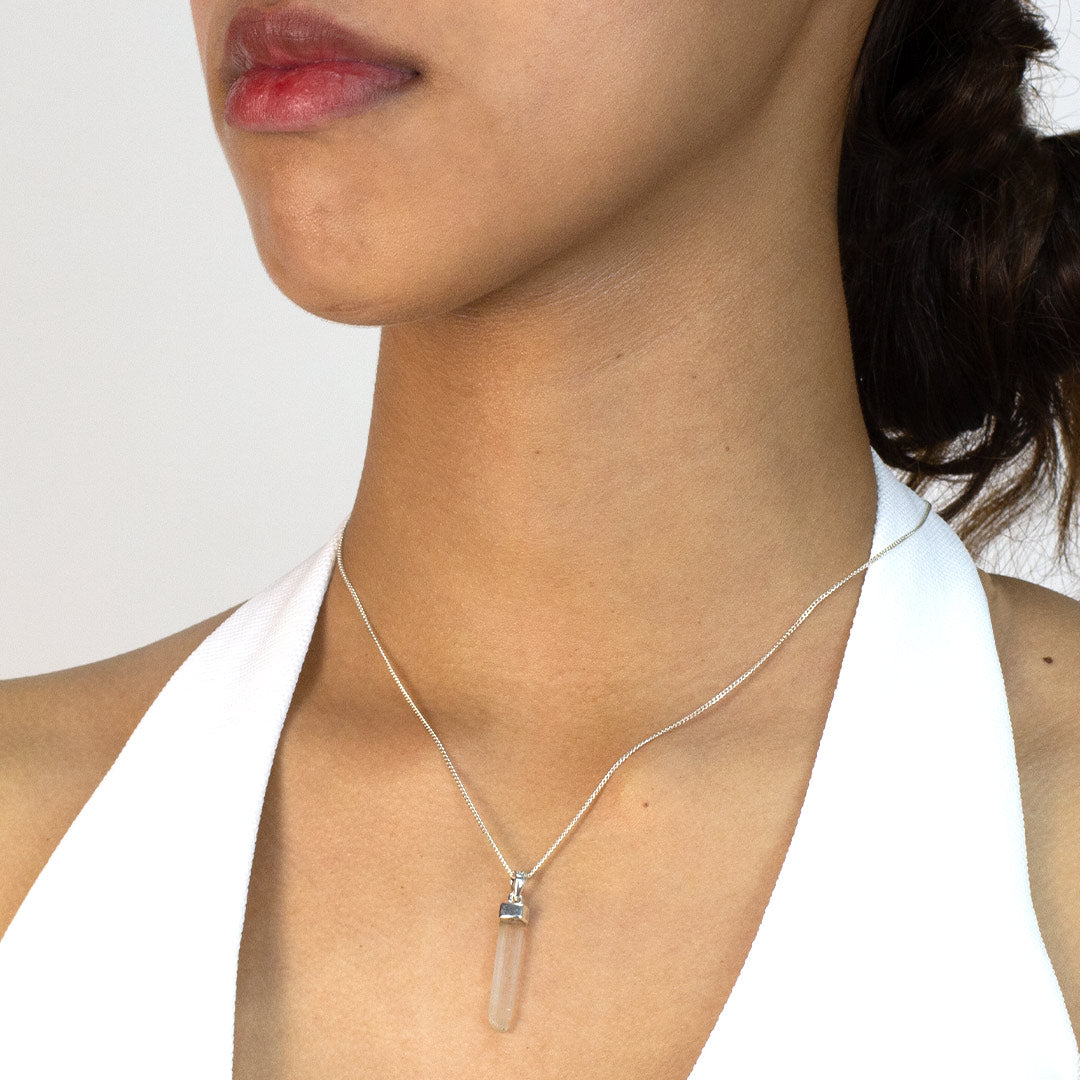 Woman wearing a necklace with a clear pendant on a plain background