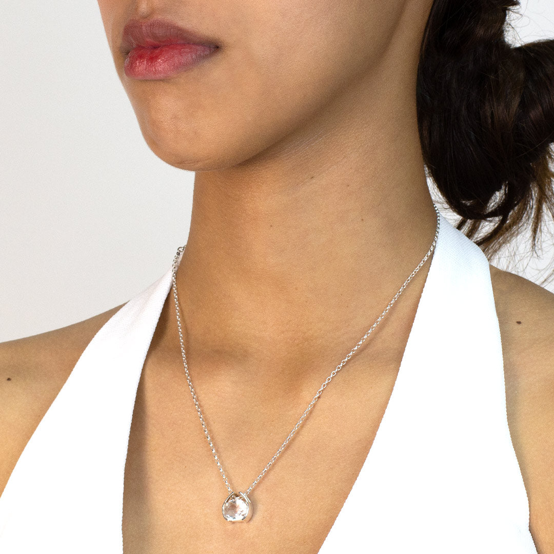 Woman wearing a silver necklace with a clear gemstone pendant on a plain background