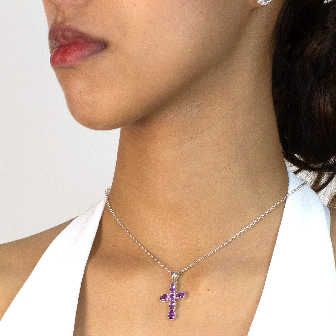 Woman wearing a purple cross pendant necklace on a plain background