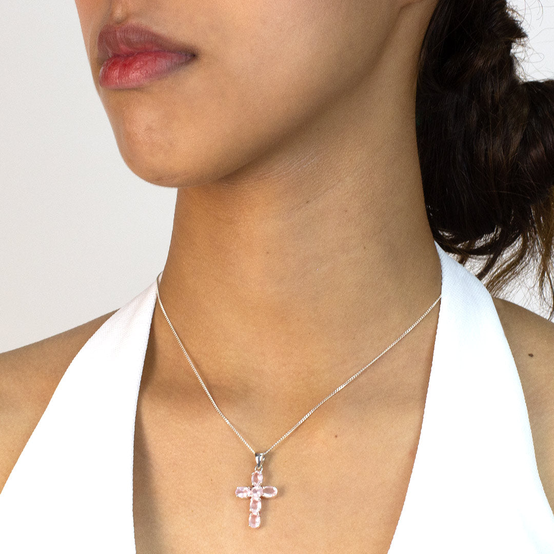 Woman wearing a pink cross pendant necklace on a plain background