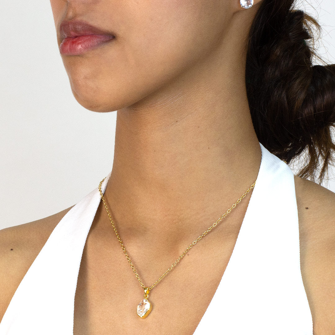 Woman wearing a gold necklace with a clear pendant on a plain background
