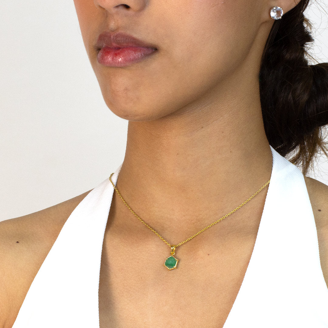 Woman wearing a gold necklace with a green gemstone pendant on a plain background