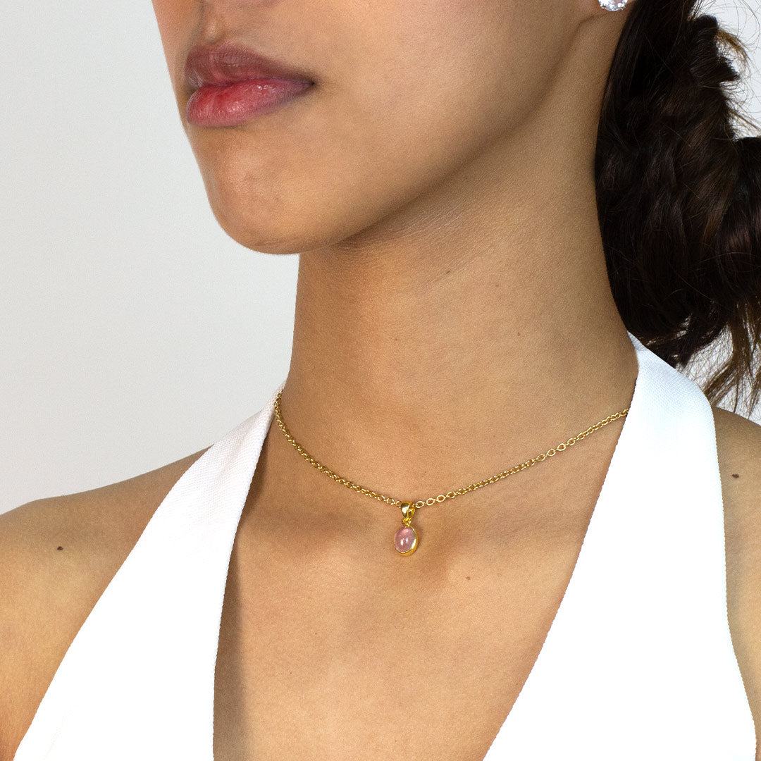 Woman wearing a gold necklace with a pink pendant on a plain background