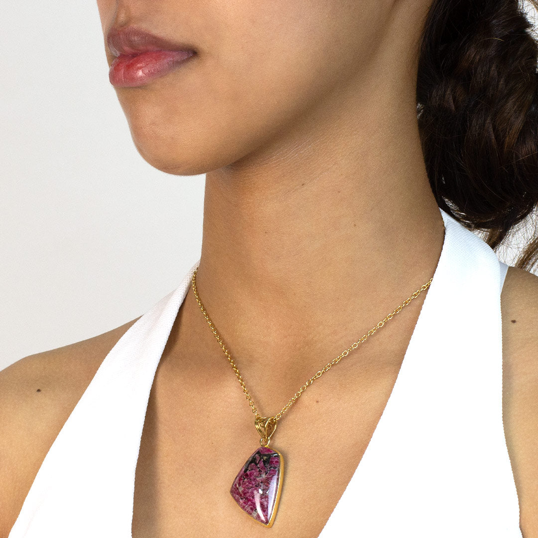 Woman wearing a gold necklace with a pink stone pendant on a white background