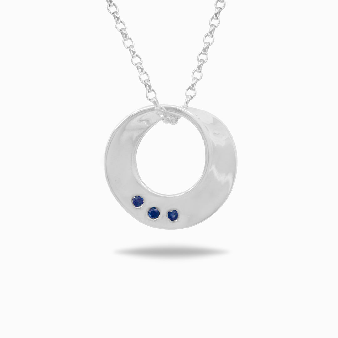 Silver necklace with a circular pendant featuring three blue stones on a white background